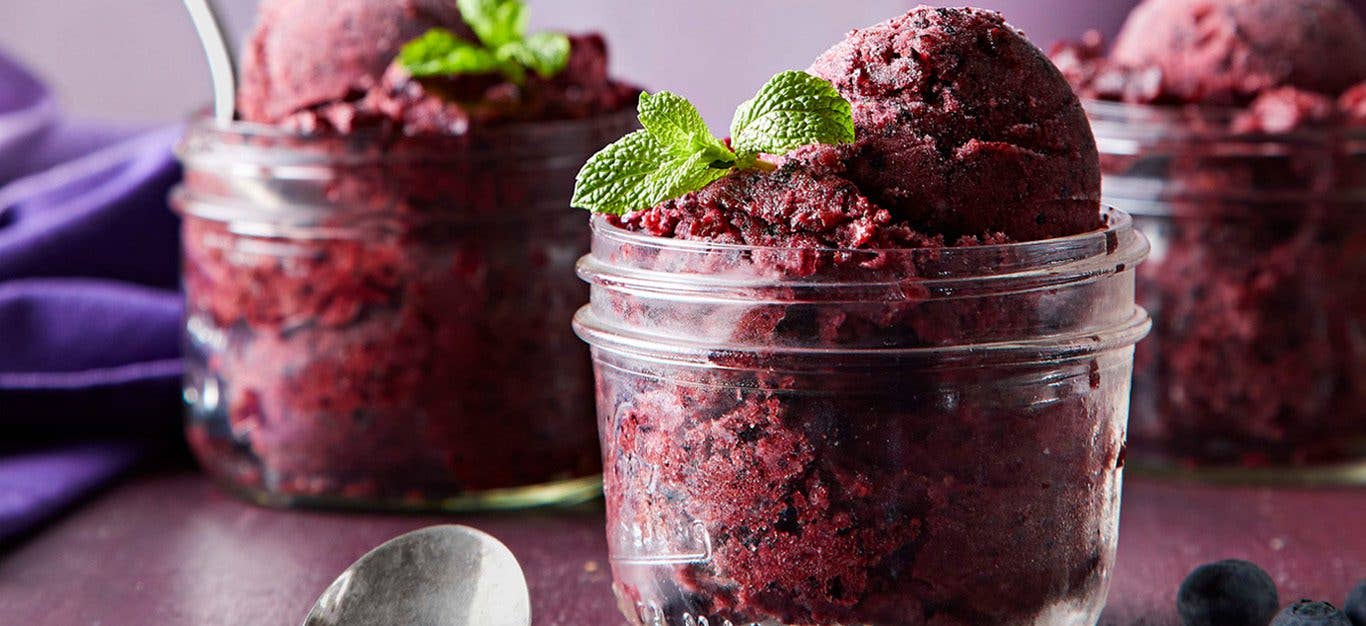 Deep purple blueberry and mint nice cream shown from the side in a clear glass Mason jar, topped with sprigs of mint - vegan ice cream recipe