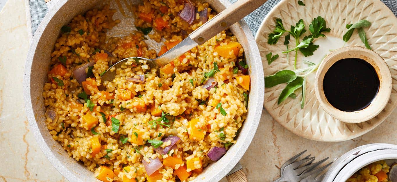 butternut squash risotto with a serving spoon next to a small bowl of balsamic vinegar