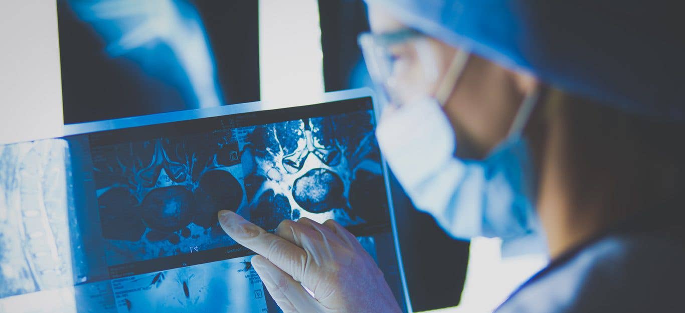 A masked doctor looks at a MRI scan