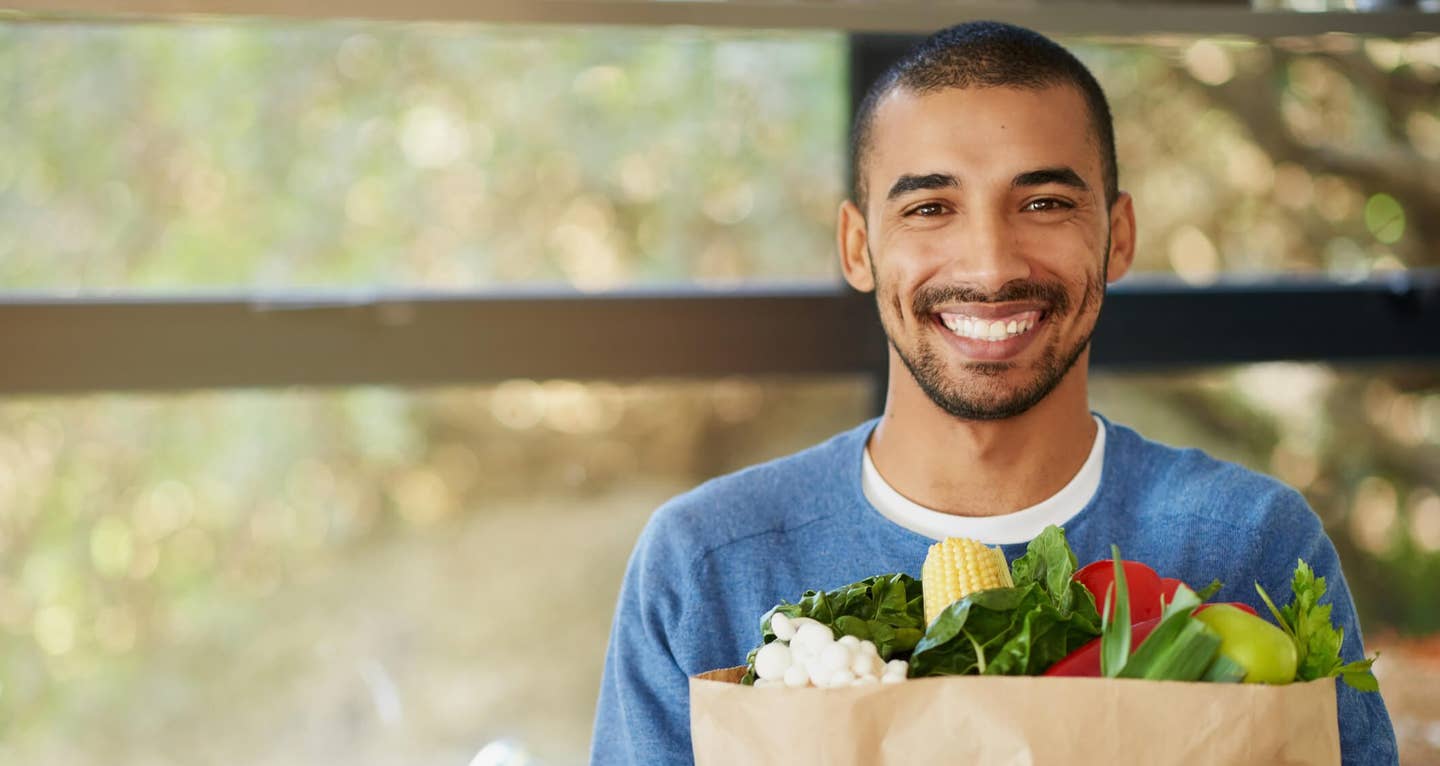 Portrait of a happy young man holding a bag full of healthy vegetables at home