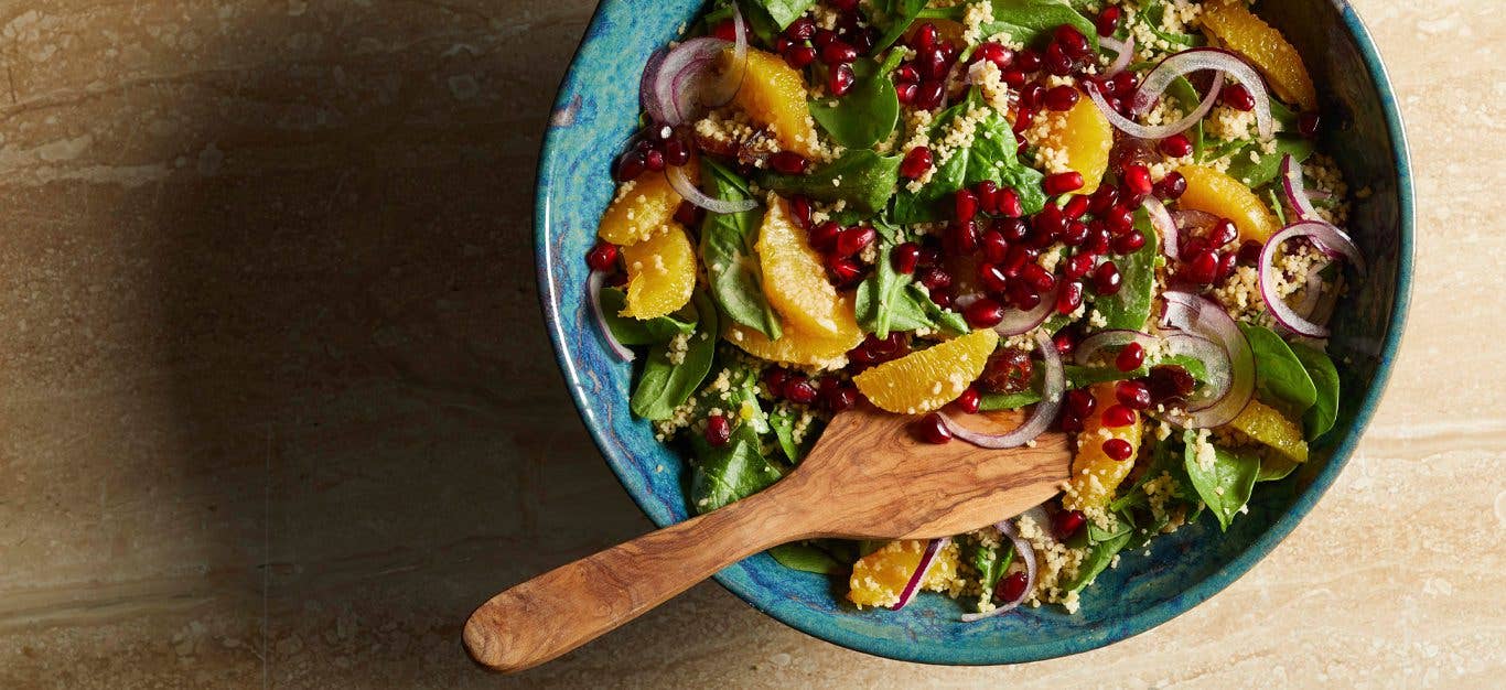 Date and Orange Couscous Salad in a blue ceramic bowl with wood serving spoon