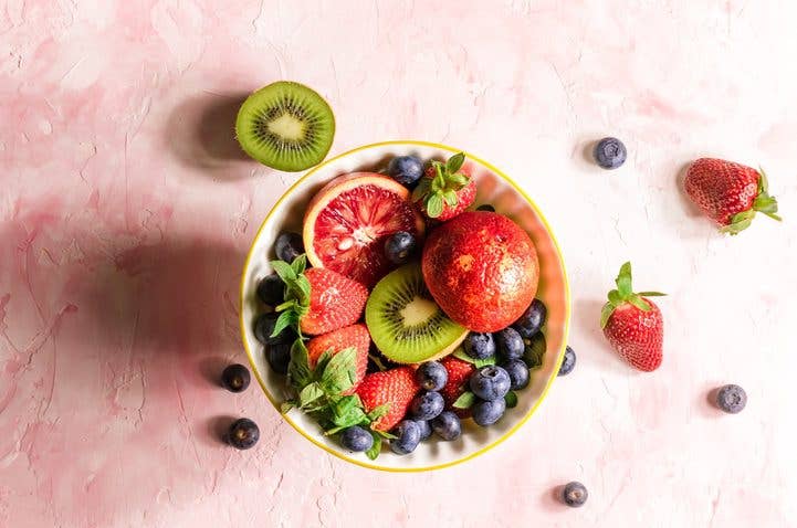 assorted fresh fruits in a bowl on a pink background