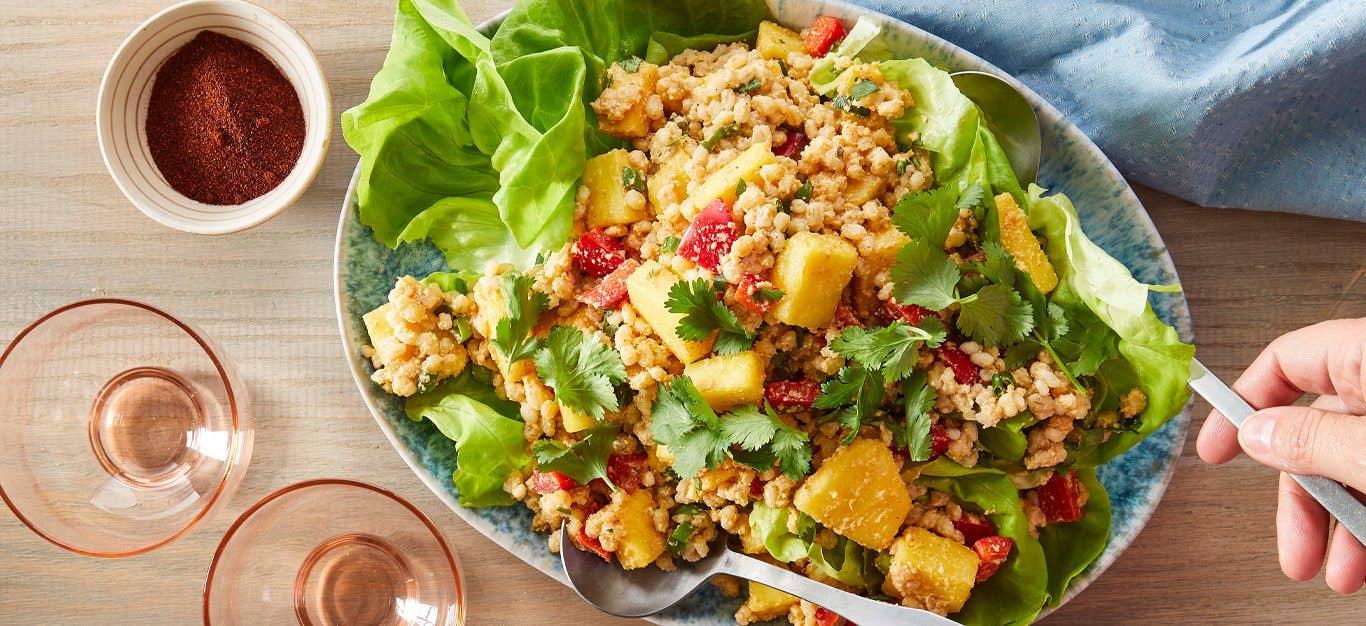 Fresh Pineapple and Barley Salad being tossed with a fork and spoon while sitting on a wood tabletop