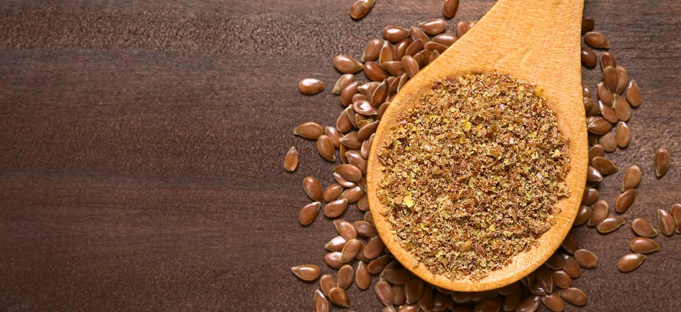 Ground and whole flaxseeds on a wooden table