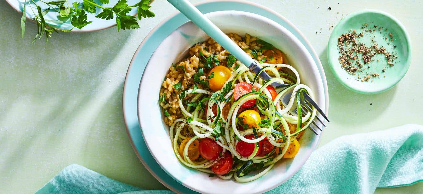 Herbed Vegan Risotto with Zoodles in a white bowl with a metal fork and blue napkin