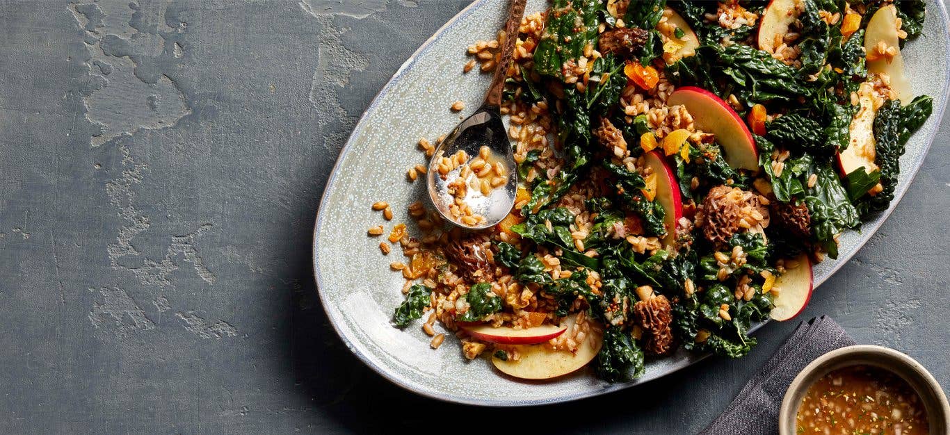 Morel Mushroom and Apple Salad with Kale on a white serving platter next to a small bowl of dressing