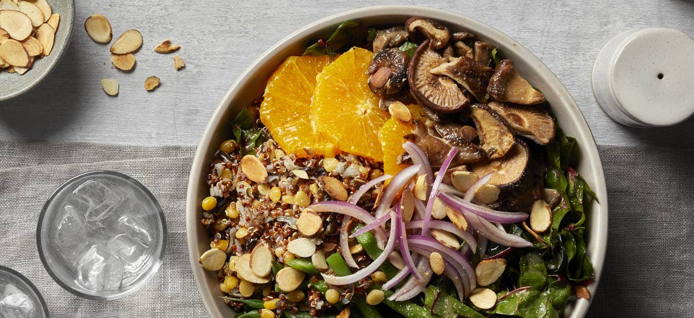 Mixed Grain Bowls with Mushrooms and Lentils on a wooden tabletop with a glass of water to the left