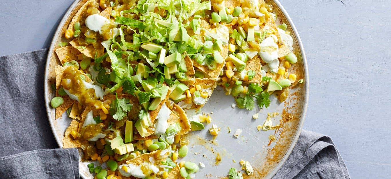 Vegan nachos verdes sprinkled wth cilantro on a gray background