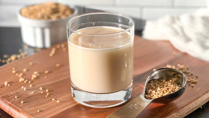 Oat milk in a clear glass on a wood cutting board