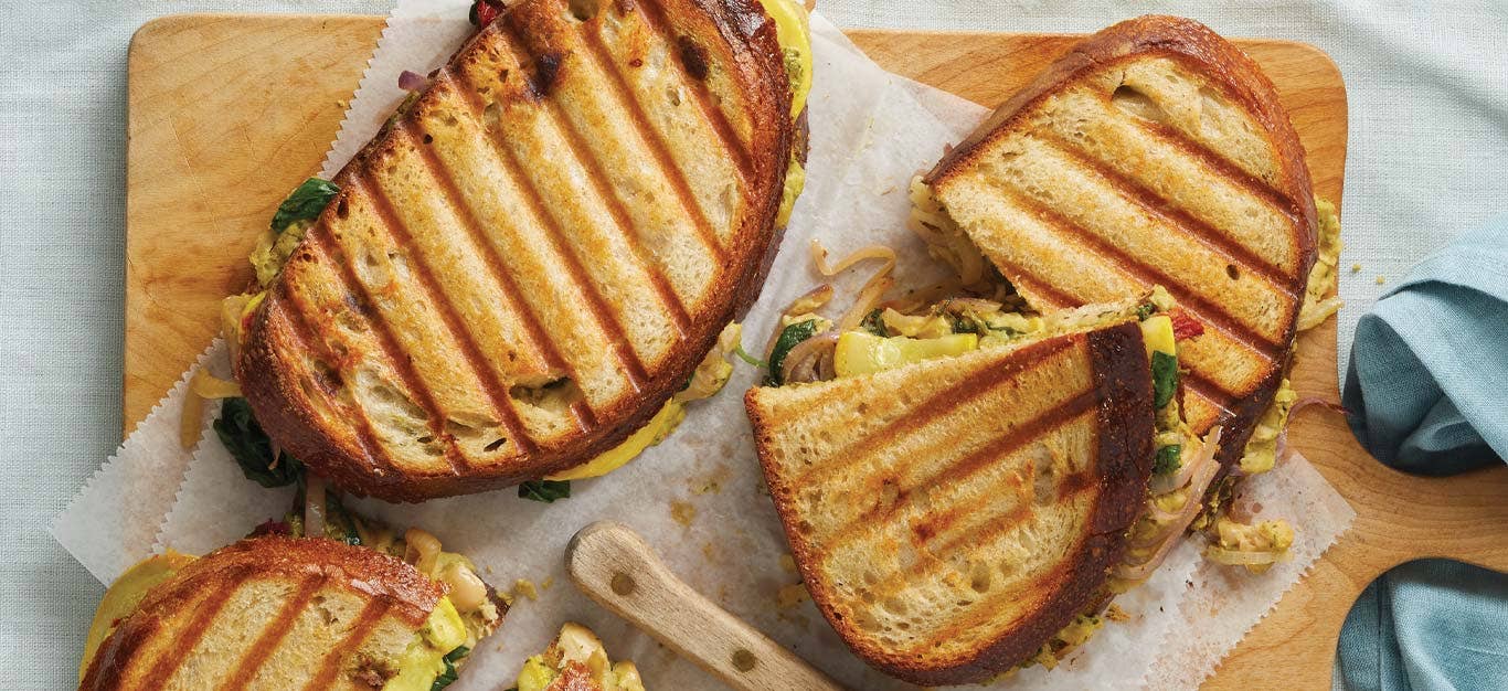 Pesto and Veggie Paninis on parchment paper on a wooden cutting board