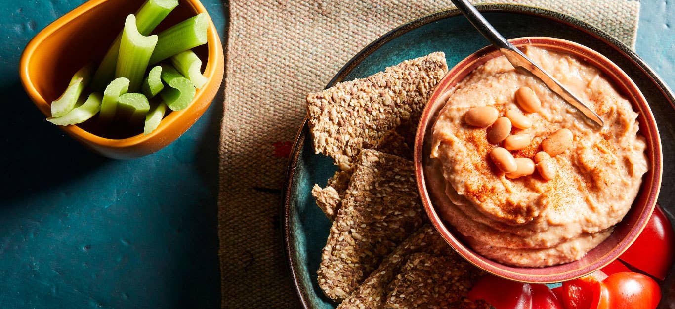 Pinto Bean Spread in a small orange bowl on a plate with crackers and celery sticks