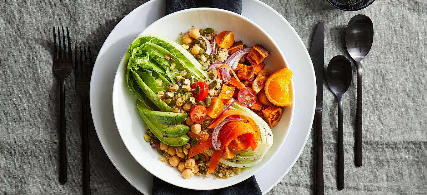 Bowl in a restaurant place setting, in the bowl is an array of whole food plant-based ingredients including chickpeas, pumpkin seeds, and tofu, layered over a heart of romaine lettuce