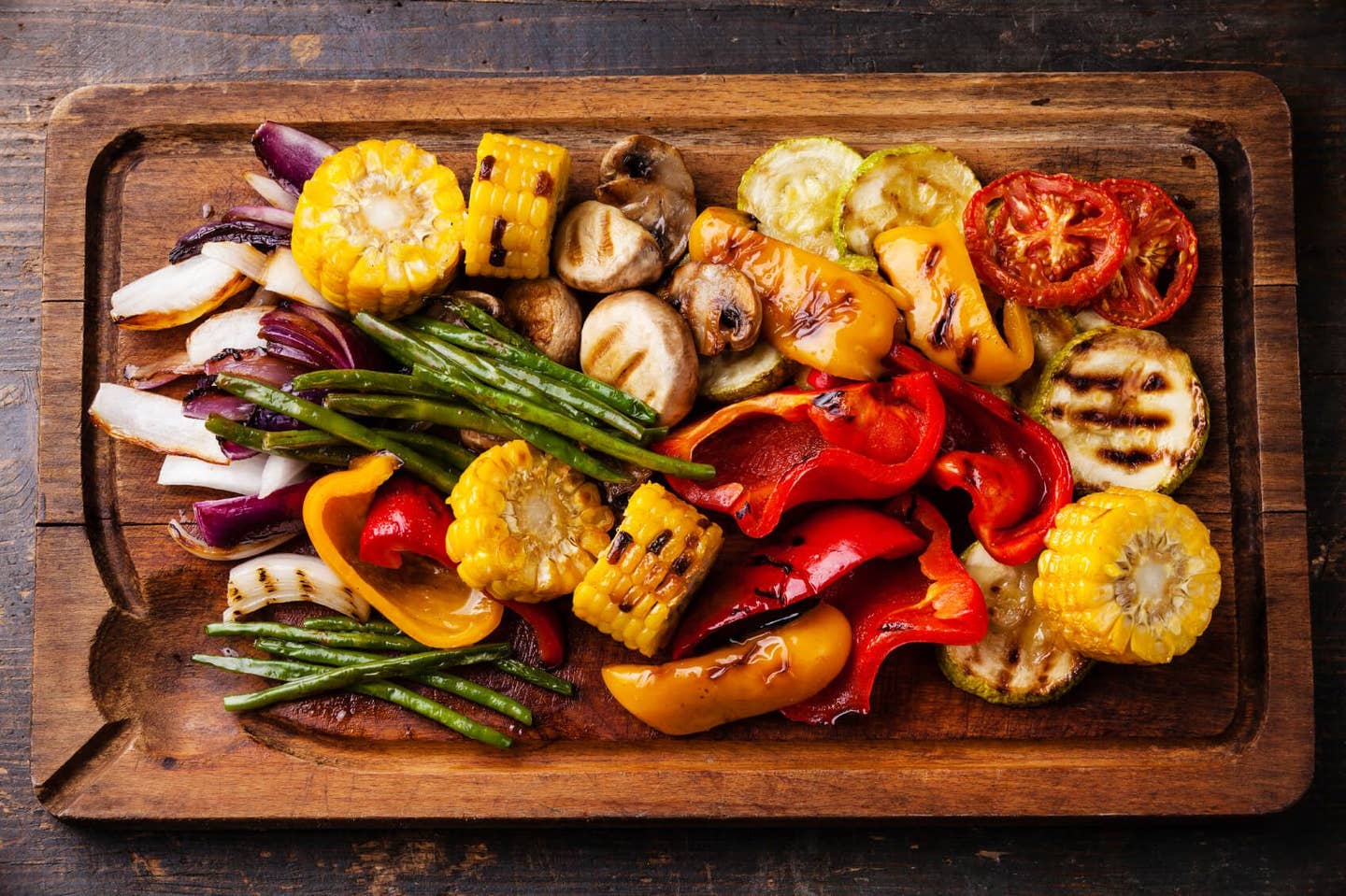 Grilled vegetables on cutting board on dark wooden background