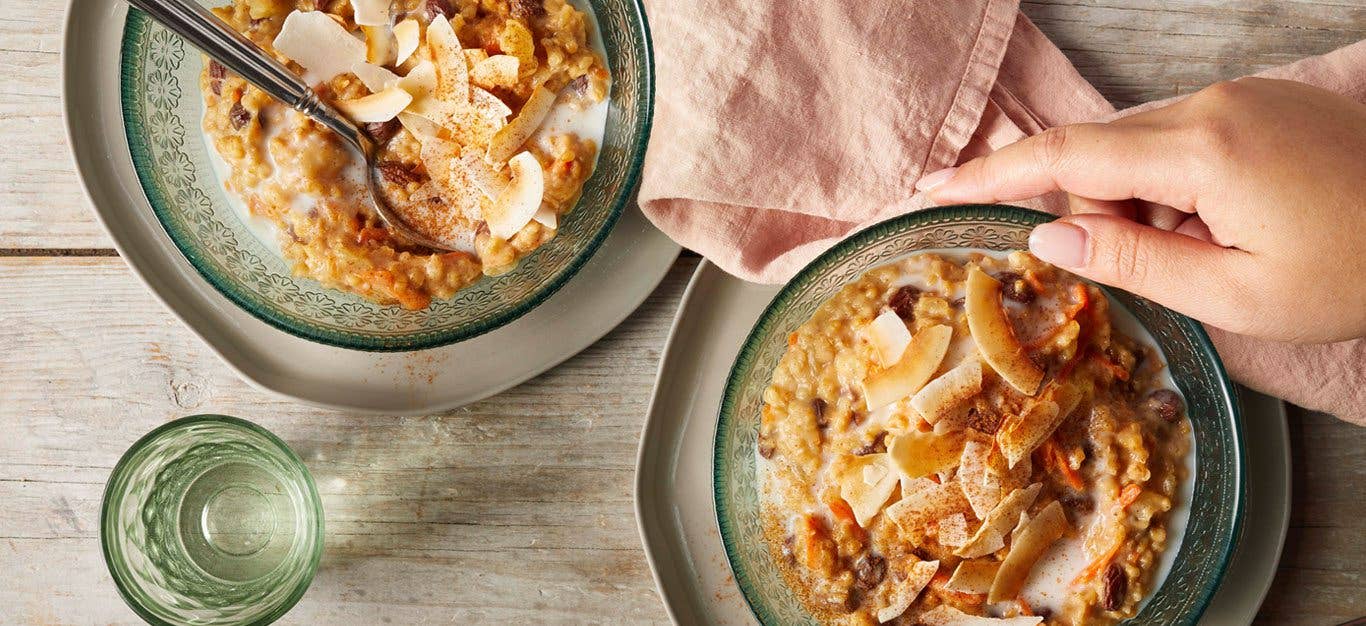 Tropical Slow-Cooker Oatmeal in blue glass bowls on a wooden table as a woman's hand reaches for one bowl