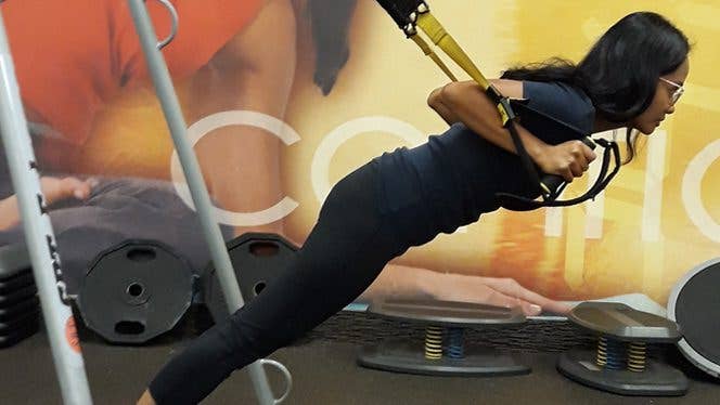 A young woman uses a trx machine to train at the gym