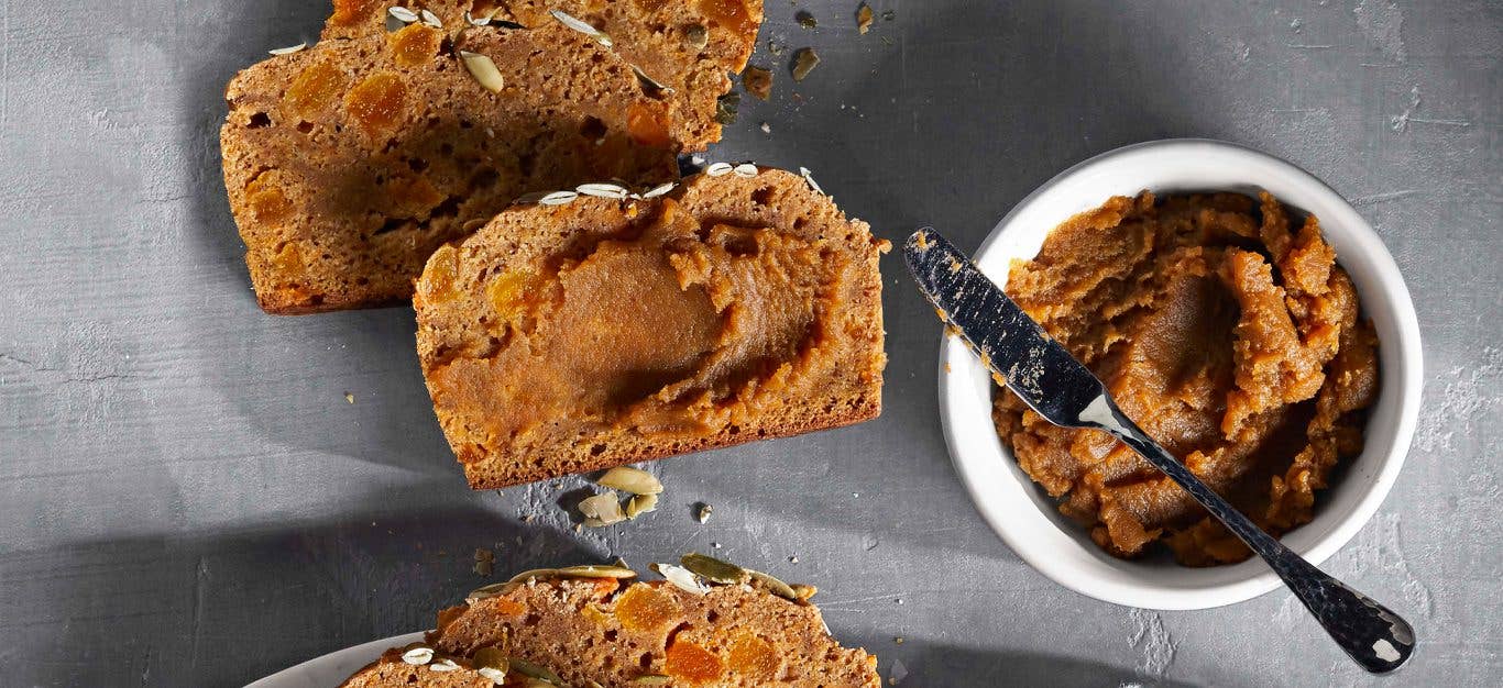 Sweet Potato Butter in a white bowl with a metal knife next to slices of bread slathered in the butter