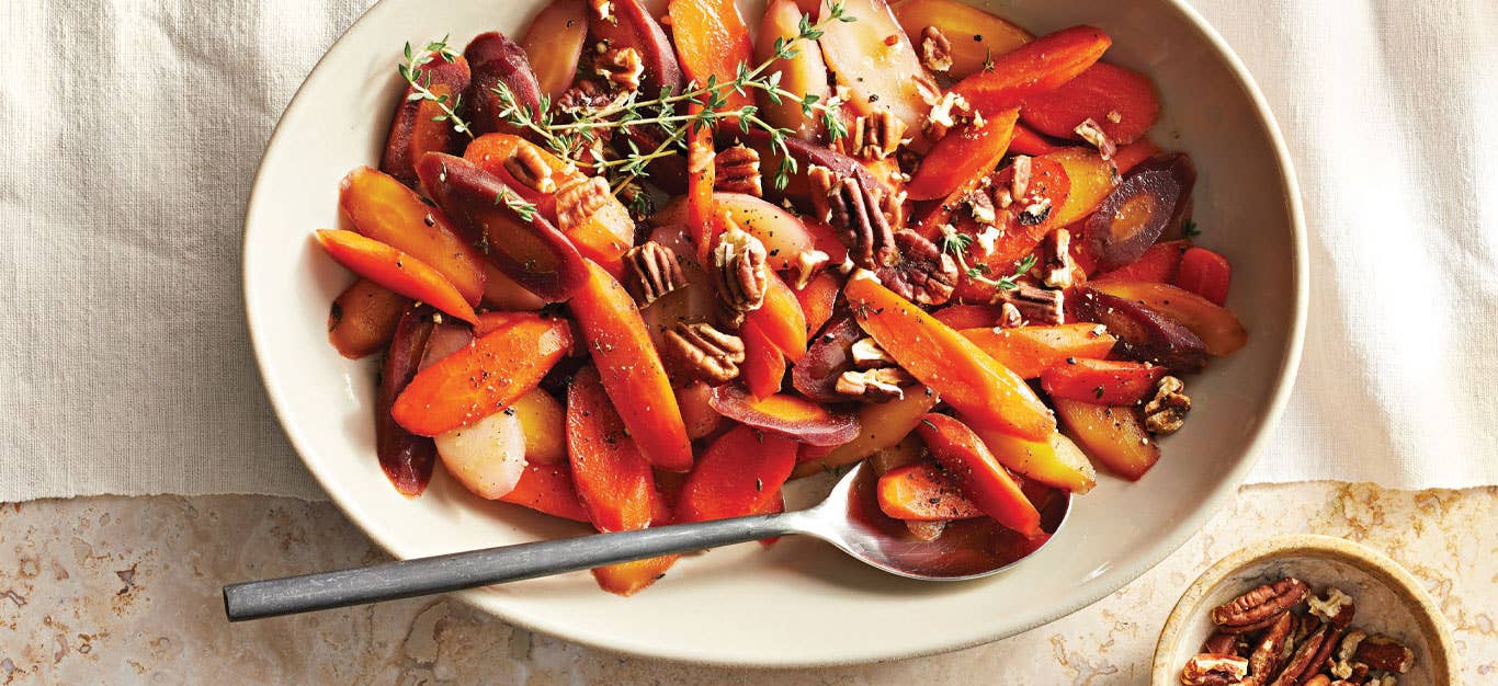 Maple-Glazed Carrots with Thyme in a white oval dish with a metal serving spoon