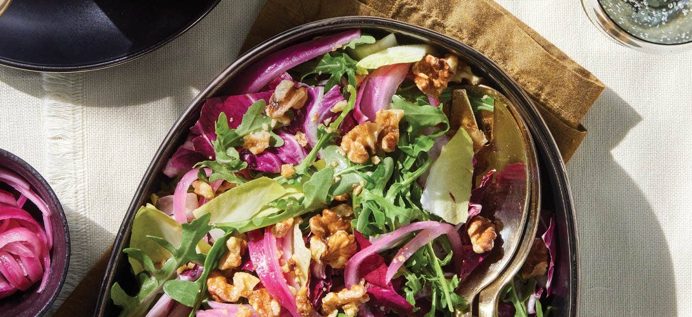 Tricolor Salad with Quick-Pickled Onions on an oval serving platter with gold metal serving spoons